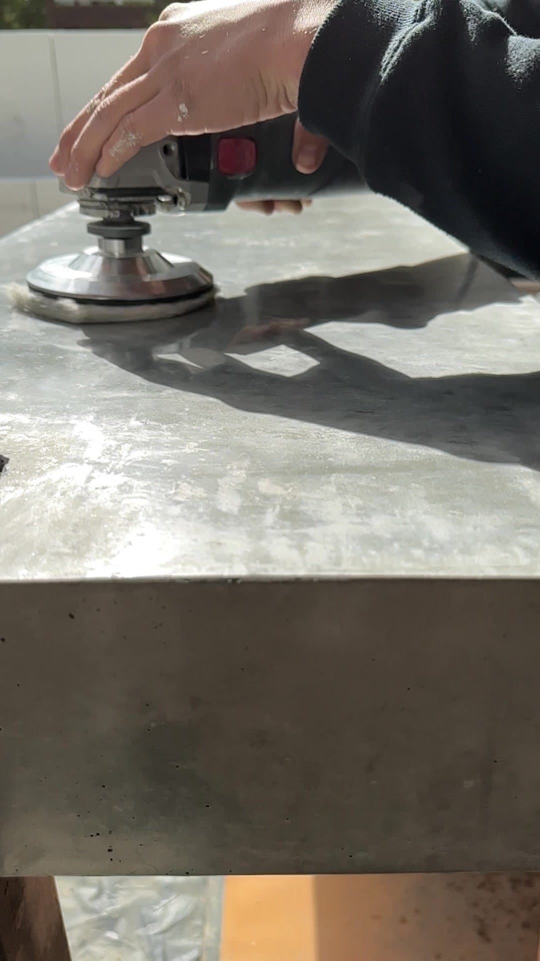 Hand polishing the top of a concrete bench with a resin pad, sunlight raking across the surface