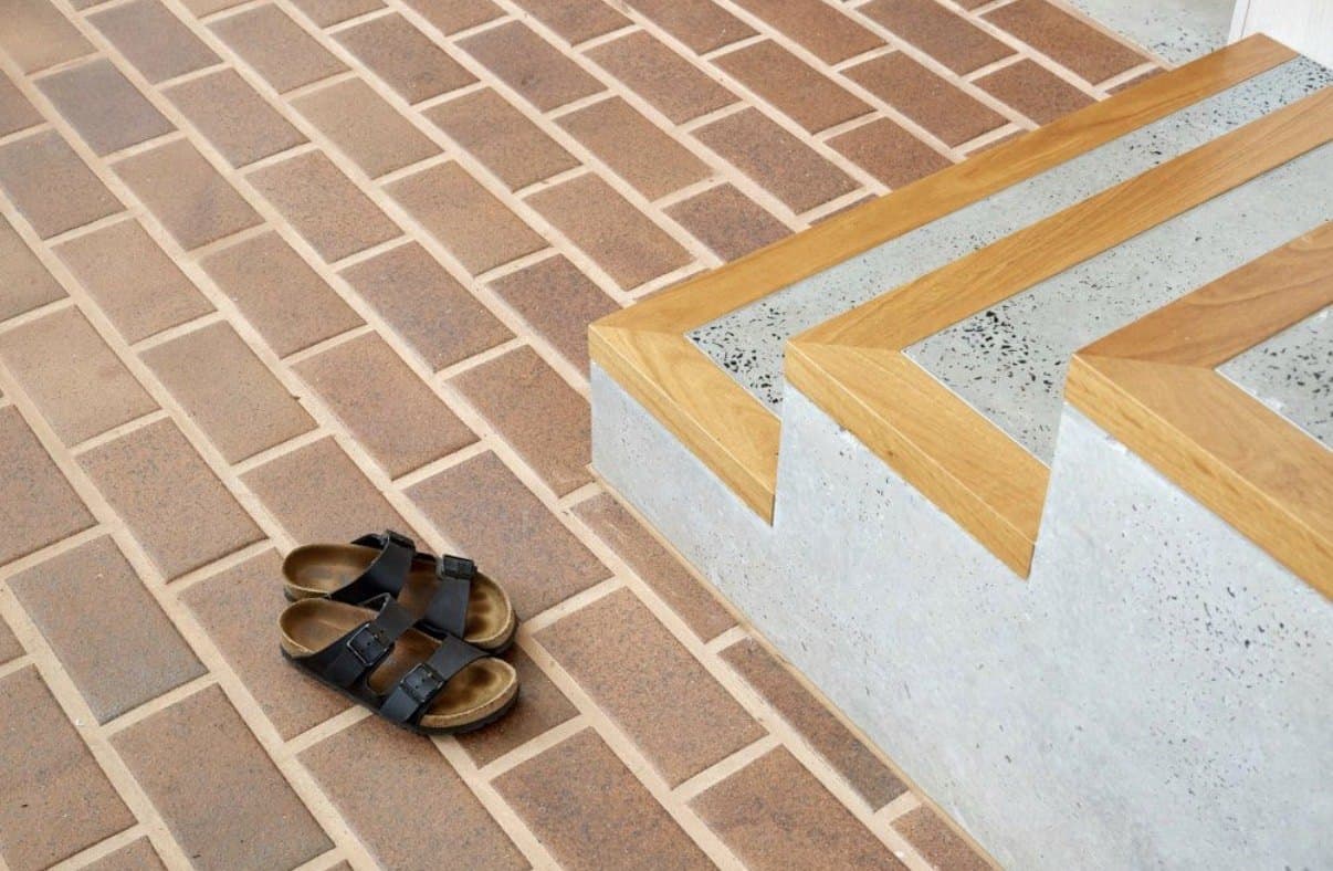 Honed concrete step with timber edge set into a brick floor